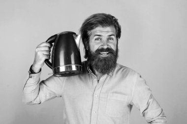 Bunu denemelisin. Mutfak konsepti Bıyıklı vahşi yakışıklı adam çay içiyor. Olgun koca elektrikli su ısıtıcısı tutar. Hayattaki modern teknoloji. Sakallı hippi ev aletleri kullanıyor..