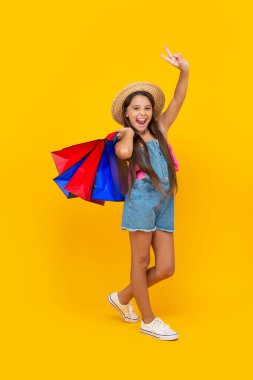 happy teen girl with shopping bags show peace on yellow background. full length.