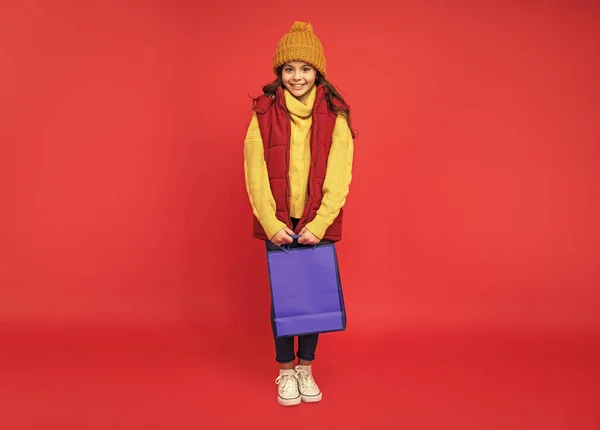 Счастливый Ребенок Зимней Шляпе Держать Сумки Покупок Красном Фоне Покупки — стоковое фото