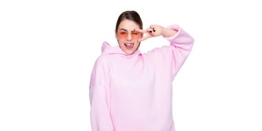 Pembe kapüşonlu, gözlüklü, dilini dışarı çıkaran mutlu bir kadın beyaz üzerine izole edilmiş barış hareketi yapıyor..