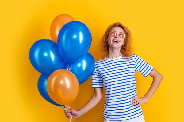 dreamy woman with birthday balloon in sunglasses. happy birthday woman hold party balloons in studio. woman with balloon for birthday party isolated on yellow background.