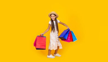 Sarı arka planda alışveriş torbaları olan pozitif bir genç kız. tam uzunluk.