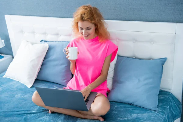 smiling woman freelancer with coffee at home chat on laptop. freelancer woman work at home. home work for freelancer. woman in bed with laptop.