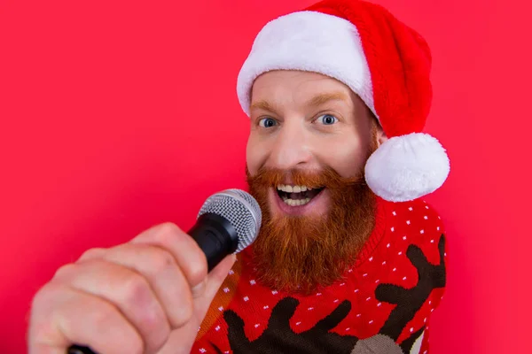 サンタハットの髭の男の肖像画がマイクと一緒に歌っている サンタクロースは赤で隔離されたクリスマスの歌スタジオを歌っています クリスマスカラオケパーティーを楽しむ クリスマスを祝う — ストック写真