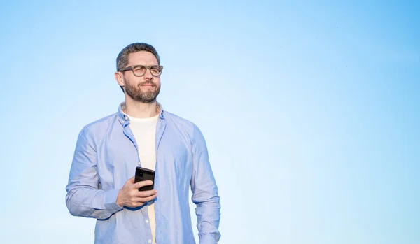 man in glasses chat on smartphone with message. man chatting on phone messaging. copy space. smartphone communication. man chat on sky background.