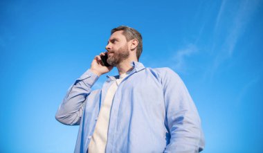Tanrı bağlantısı. Telefonda erkek erkeğe konuşma. Adam akıllı telefondan konuşuyor. Gökyüzü arka planında insan iletişimi.