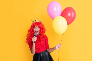 Sarı arka planda mikrofon ve parti balonuyla tacın içinde gülümseyen çocuk..