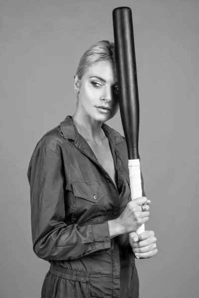 looking away. rounders game. woman in boilersuit with bat. female baseball player. sports and games. cricket player on orange background. lady girl holding sport equipment or accessory. active wear.