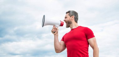 man in red shirt shout in loudspeaker on sky background.