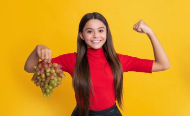 Güçlü çocuk sarı arka planda taze üzüm tutar..