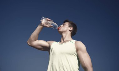 Mavi gökyüzü üzerinde yeşil tshirt atlet. Spor ve fitness kavramı. Vücut kas el kasları pazı, triceps ile. Sağlıklı yaşam ve sağlık. Adam içme suyu şişe güneşli.
