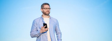 Gözlüklü adam akıllı telefondan fotokopi odasıyla sohbet ediyor. Adam telefonda mesajlaşıyordu. Akıllı telefon iletişimi. Adam gökyüzü arka planında sohbet ediyor.