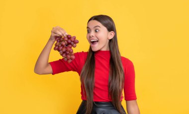 Afallamış çocuk sarı arka planda bir demet üzüm tutuyor..