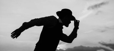 Dans pozu. Bunu başarabilirsin. İnsan motivasyonu hisseder. Gökyüzü arka planında şapka silueti olan iş adamı. Güven ve başarı. Başarılı gelecek kavramı. Erkek dansçı açık havada dans ediyor.