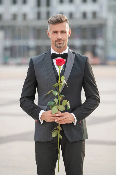 elegant man in tuxedo at romantic occasion. man with romantic present. grizzle romantic man with rose.