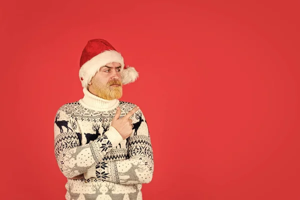 bearded hipster dyed hair red background. new year party is here. copy space. christmas shopping time. mature male knitted xmas sweater. brutal man hate winter holidays. serious man santa hat.