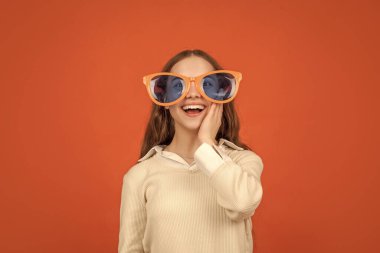 going crazy. childhood happiness. fancy party look. happy funny kid in glamour eyeglasses on orange background. funky teen girl having fun. cheerful child in party glasses. fashion accessory.