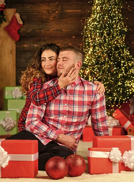 receiving Christmas gifts. Enjoying spending time together in New Year Eve. Couple in love sit next to Christmas tree. hugging among present boxes. romantic couple is having fun. evening before xmas.
