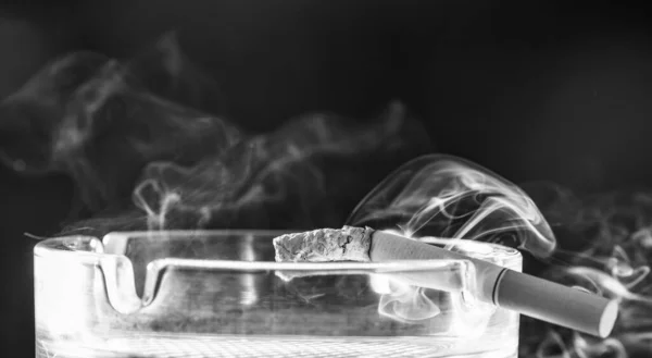 Tobacco or health. Burning cigarette in glass ashtray. Tobacco smoking. Smoke rising from cigarette in ash-tray. Bad habit. Nicotine addiction.