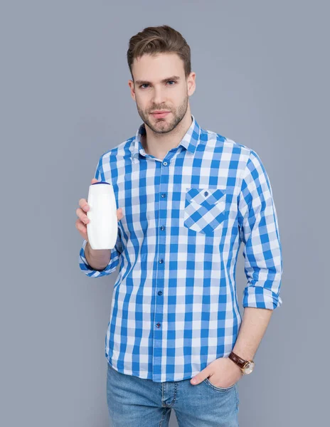 young guy hold bottle of aftershave product. guy hold aftershave product isolated on grey background. guy with aftershave product in studio. aftershave product for guy.