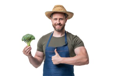 Önlüklü ve şapkalı bir adam, beyaz üzerine izole edilmiş brokoli sebzeli. başparmak yukarı.