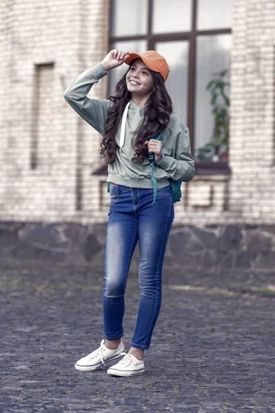 Stylish little girl fix cap with fashion look wearing casual clothes on urban outdoors, style.