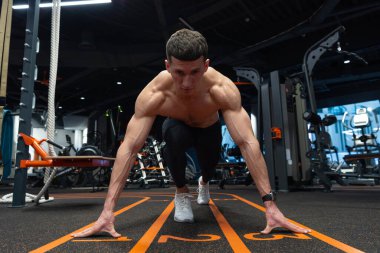 Spor salonunda başlangıç çizgisinde çömelmiş bir koşucu. Atletik adam koşu için başlangıç pozisyonunda. Spor salonunda atlet eğitimi. Spor salonunda antrenman yapmak. Spor ve zindelik.
