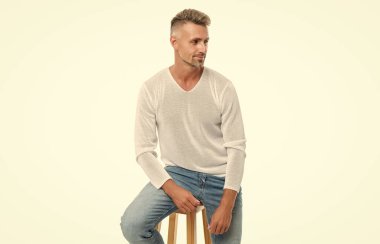 Gülümseyen, beyaz saçlı, olgun, yakışıklı bir adam beyaz arka planda izole edilmiş bir sandalyeye oturuyor..