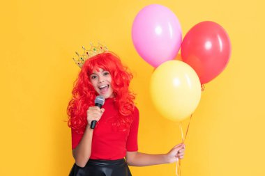 Sarı arka planda parti balonu ve mikrofonla taç takmış çocuk gülümsemesi..