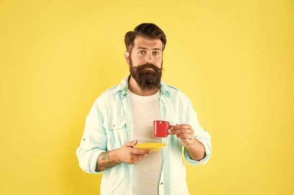 Serious guy drinking coffee from cup holding saucer yellow background, break.