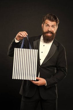 cheerful man in tuxedo bow tie formalwear on black background with shopping bag. birthday. copy space.