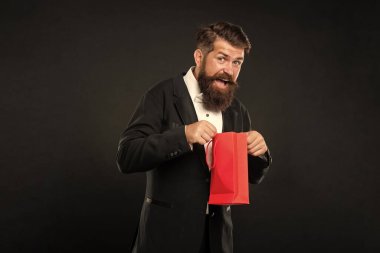 Smokinli, papyonlu, siyah arka planda açık alışveriş çantası takan meraklı bir adam..