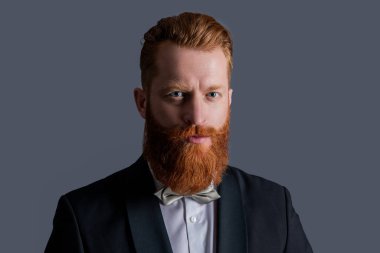 Smokin giymiş bir adamın stüdyosunun yüzü. Zarif smokin giyen bir adam. Smokin modası. Smokinli yakışıklı sakallı adam gri arka planda izole edilmiş..