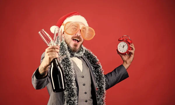 Time to celebrate new year. Christmas party. Man bearded hipster santa hat champagne bottle. alarm clock. Corporate party. Cheers concept. Join office party. Winter party ideas. Almost midnight.