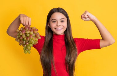 pozitif çocuk taze üzümleri sarı arka planda tutar.