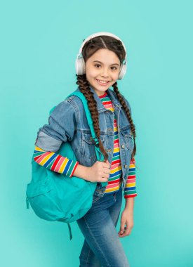 Mutlu genç kız kulaklıkla müzik dinliyor mavi arka plan, eğitim. Gayri resmi eğitim. Okul eğitimi.