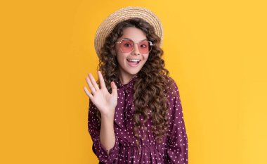 Hasır şapkalı ve güneş gözlüklü mutlu çocuk. Sarı arka planda uzun sarı kıvırcık saçlı..