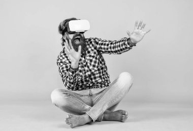 Damalı gömlekli, modaya uygun saç stiline sahip beyaz, yetişkin bir hippi video gözlükleriyle sanal oyun oynuyor..