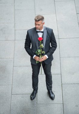 Smokinli şık bir adam. Dışarıda papyon giyen bir adam. Kırmızı güllü romantik smokinli adam..