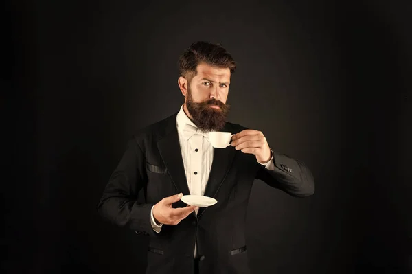man in tuxedo bow tie with coffee cup. gentleman in formalwear drink coffee on black background.