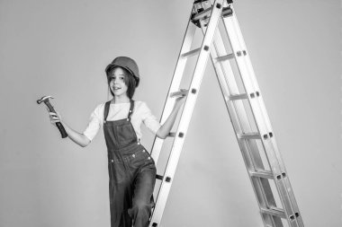 Çocuk mimar. Mühendis çekiç kullanıyor. İşçi çocuk güvenlik kaskı takıyor. İşçi bayramı. Üniformalı ve kasklı merdivenli genç bir kız. Sert şapkalı kadın müteahhit. bina ve inşaat.