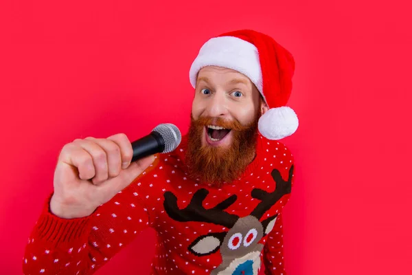 christmas music party. happy man at christmas music party with microphone. christmas santa man at music party isolated on red background.