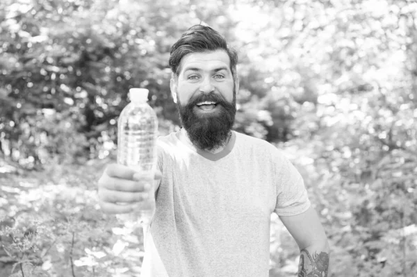 happy bearded man with beard in summer clothes offering water bottle in forest, selective focus, per day.