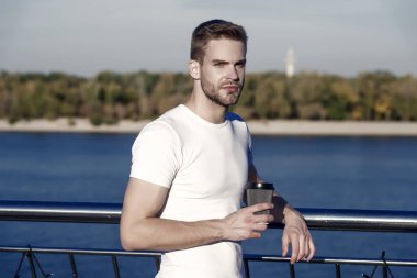 Kahveyi yanına al. Genç adam dışarıda kahve içer. Yakışıklı adam servis bardağını tut. Riber kıyısında bekâr bir adam. Sıradan tarzda traşsız bir adam. Yazlık gardırop. Moda ve tarz.