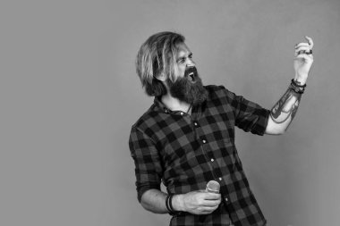Karaoke konsepti. Kareli gömlekli sakallı adam şarkı söylüyor. Sıradan bir adam şarkı söylerken insani duygularını ifade eder. Mikrofonlu duygusal hipster. Mikrofonlu erkek şarkıcı. Müziği başlat..