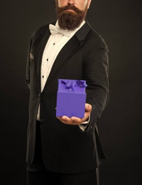 cropped gentleman in tuxedo bow tie formalwear on black background with gift box. boxing day.