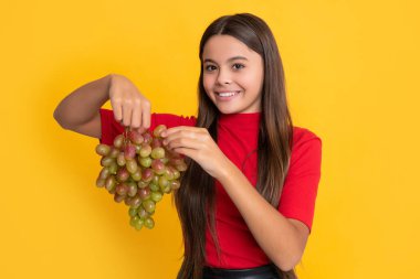 Mutlu çocuk sarı arka planda taze üzüm meyvesi tutuyor..