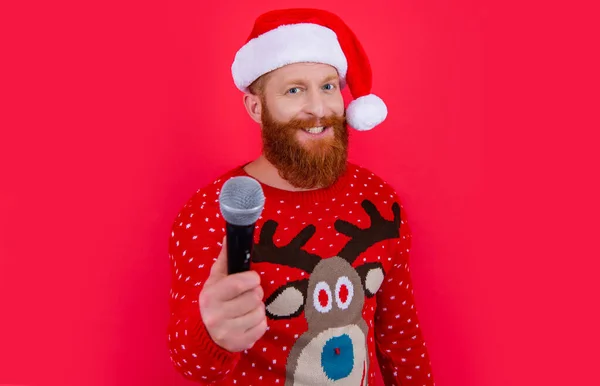 christmas music party. cheerful man at christmas music party with microphone. christmas santa man at music party isolated on red background, selective focus.