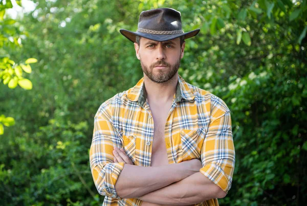 man crossed hands in cowboy hat. sexy man in checkered shirt. western man wearing hat.