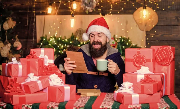 Wrapped gifts with ribbons and bows. Hipster prepared gifts for family. Fulfill cherished dreams. Man bearded santa claus hat reading letters. Generous new year. Lot of gifts. Happy winter holidays.